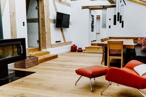 A modern interior with a flat-screen TV mounted on a white wall, wooden flooring, a dining area with a table and chairs, and a red cushioned bench. - Jura Chalet Eggersberg (Obereggersberg)
