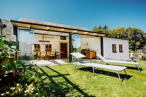 A modern house with a glass-enclosed patio, a dining area, and two lounge chairs.