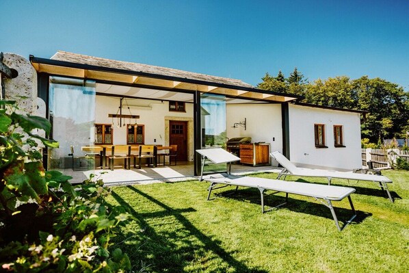 A modern house with a glass-enclosed patio, a dining area, and two lounge chairs.