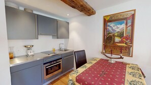 Eine Küche mit grauen Schränken, einer Edelstahl-Arbeitsplatte, einer Spüle und einem Backofen. Ein Tisch mit roter und gelber Tischdecke und einem Kerzenhalter sind ebenfalls vorhanden.
