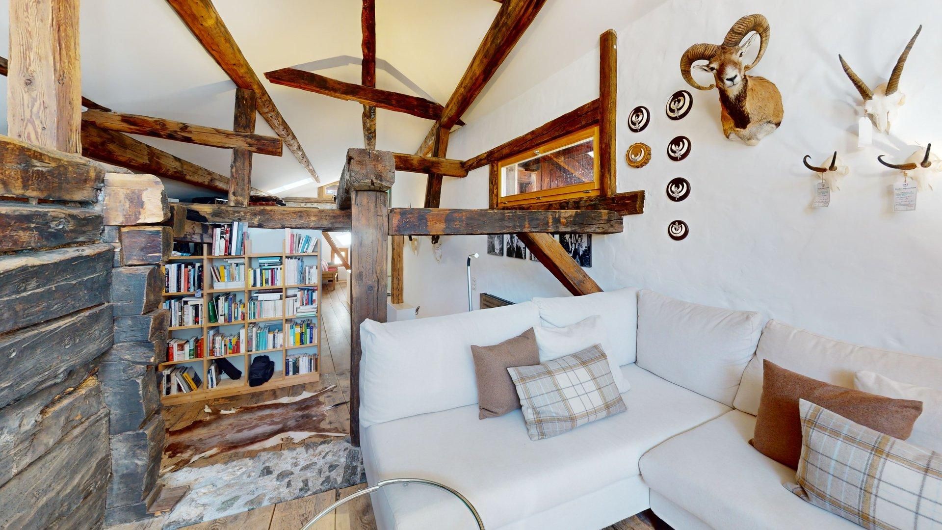 Ein rustikales Interieur mit freiliegenden Holzbalken, einem weißen Sofa, einem Bücherregal und aufgehängten Tierhörnern.