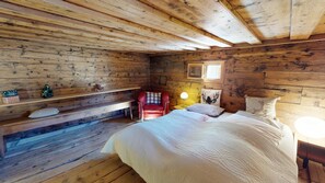 Ein Zimmer einer Holzhütte mit einem Bett, einem Sessel, einem Nachttisch und einem Fenster.