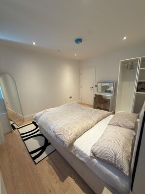 Een slaapkamer met een bed, een bureau, een kledingkast en een spiegel.