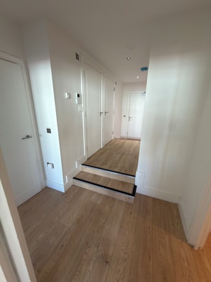 A hallway with wooden flooring, white walls, and a door at the end. - Modern 3 Bedroom Flat on Eltham High Street| 7 mins from the Station! (London)