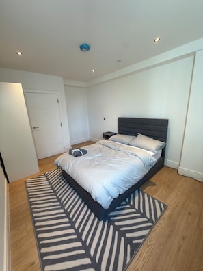 A bedroom with a bed, bedside tables, a door, and a ceiling light. - Modern 3 Bedroom Flat on Eltham High Street| 7 mins from the Station! (London)