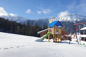 A wooden play structure with a slide and swing set in a snowy landscape with mountains in the background. - Holiday home in Pfronten with swimming pool (Pfronten)