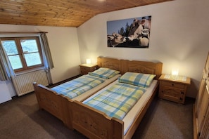 Une pièce avec un lit en bois, deux tables de chevet, une fenêtre et un tableau au mur.