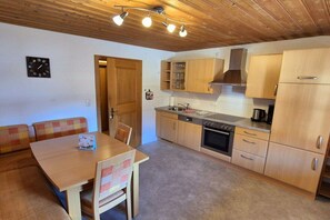 A compact kitchen with wooden cabinets, a built-in oven, and a dining area with a table and chairs. - Holiday home in Pfronten with swimming pool (Pfronten)