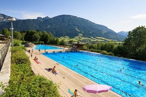 A swimming pool with a view of mountains, surrounded by greenery and a wooden deck. - Holiday home in Pfronten with swimming pool (Pfronten)