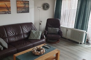 Ein Wohnzimmer mit einem braunen Ledersofa, einem Couchtisch mit einem Dekorationsobjekt, einer Stehlampe und einer Heizung.