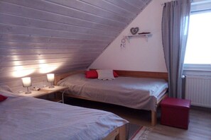 A bedroom with two beds, a small table, and a red stool. - Holiday home in Hooksiel with swimming pool (Hooksiel)