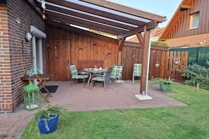 A covered patio with a table and chairs, a wooden fence, and a brick wall. - Holiday home in Hooksiel with swimming pool (Hooksiel)