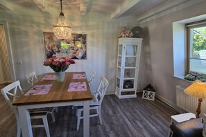 A dining area with a wooden table, white chairs, a chandelier, and a cabinet with glass doors. - Holiday home in Cuxhaven with swimming pool (Cuxhaven)