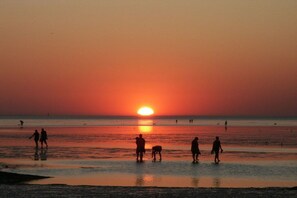 A sunset over a beach with people and a dog. - Holiday home in Cuxhaven with swimming pool (Cuxhaven)