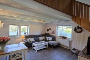 A cozy living room with a wooden staircase, a black leather sofa, a white coffee table, and a view of the outdoors through a window. - Holiday home in Cuxhaven with swimming pool (Cuxhaven)