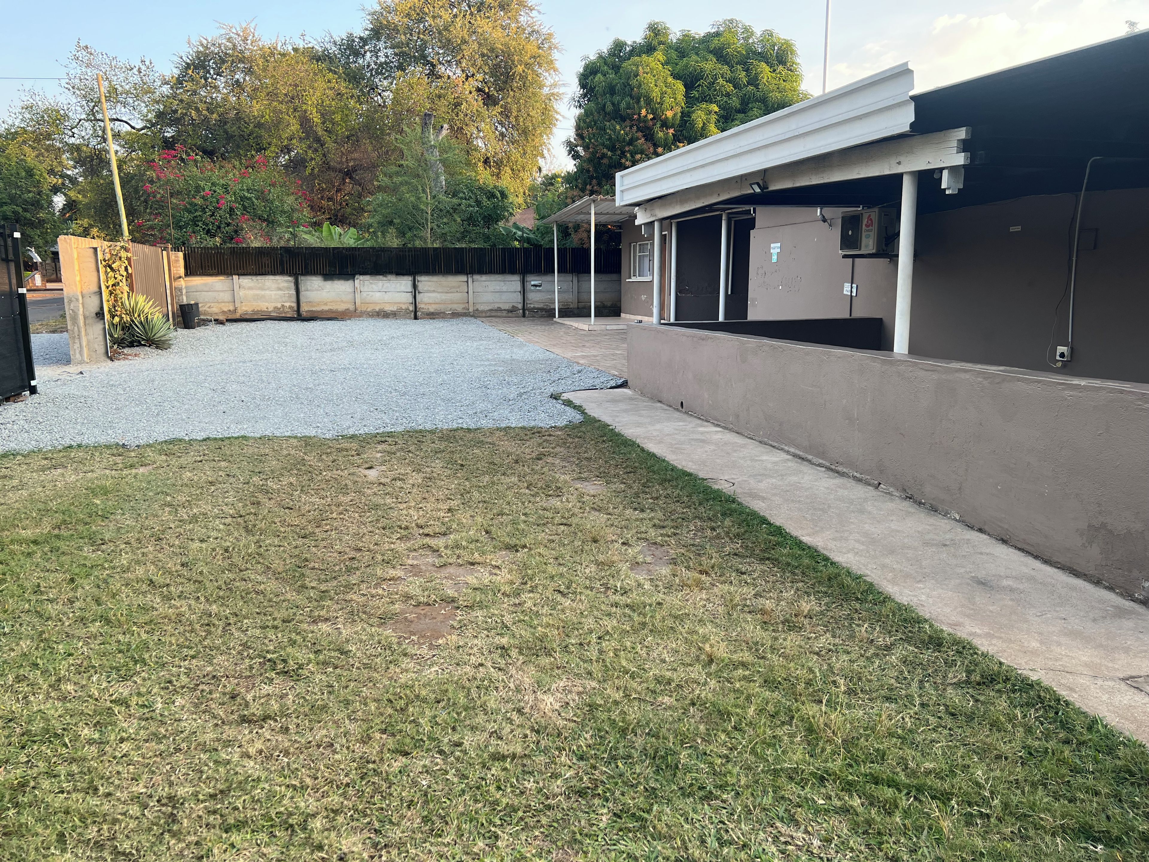 A building with a covered outdoor area, a gravel driveway, and a grassy lawn.