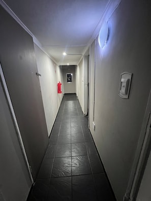 Un passadís estret amb sòl de rajoles, un extintor de foc fixat a la paret i una porta al final.