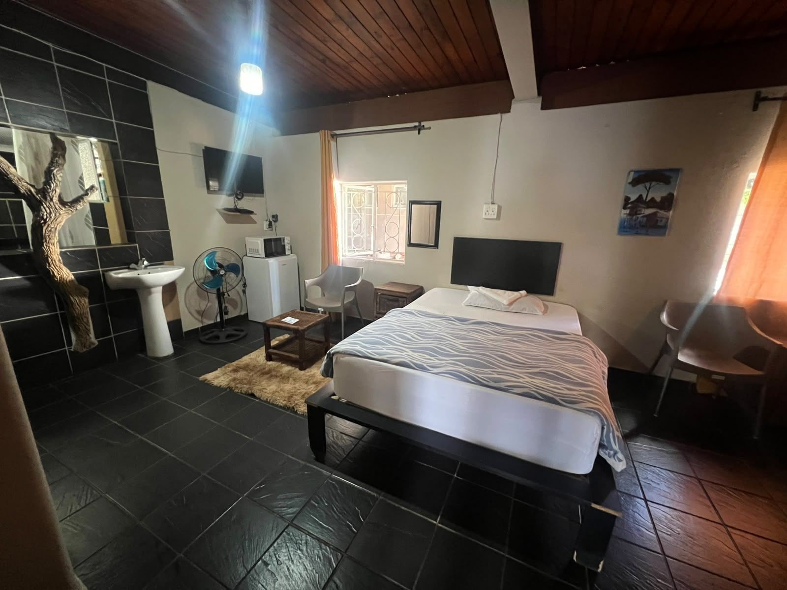 Un dormitorio con cama, escritorio, silla, lavamanos y ventilador.