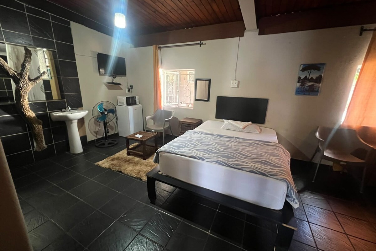 A bedroom with a bed, a desk, a chair, a sink, and a fan.