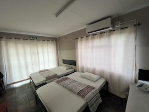A hotel room with two beds, a flat-screen TV, an air conditioning unit, and a curtain. - Happy Time Guest House  (Phalaborwa)