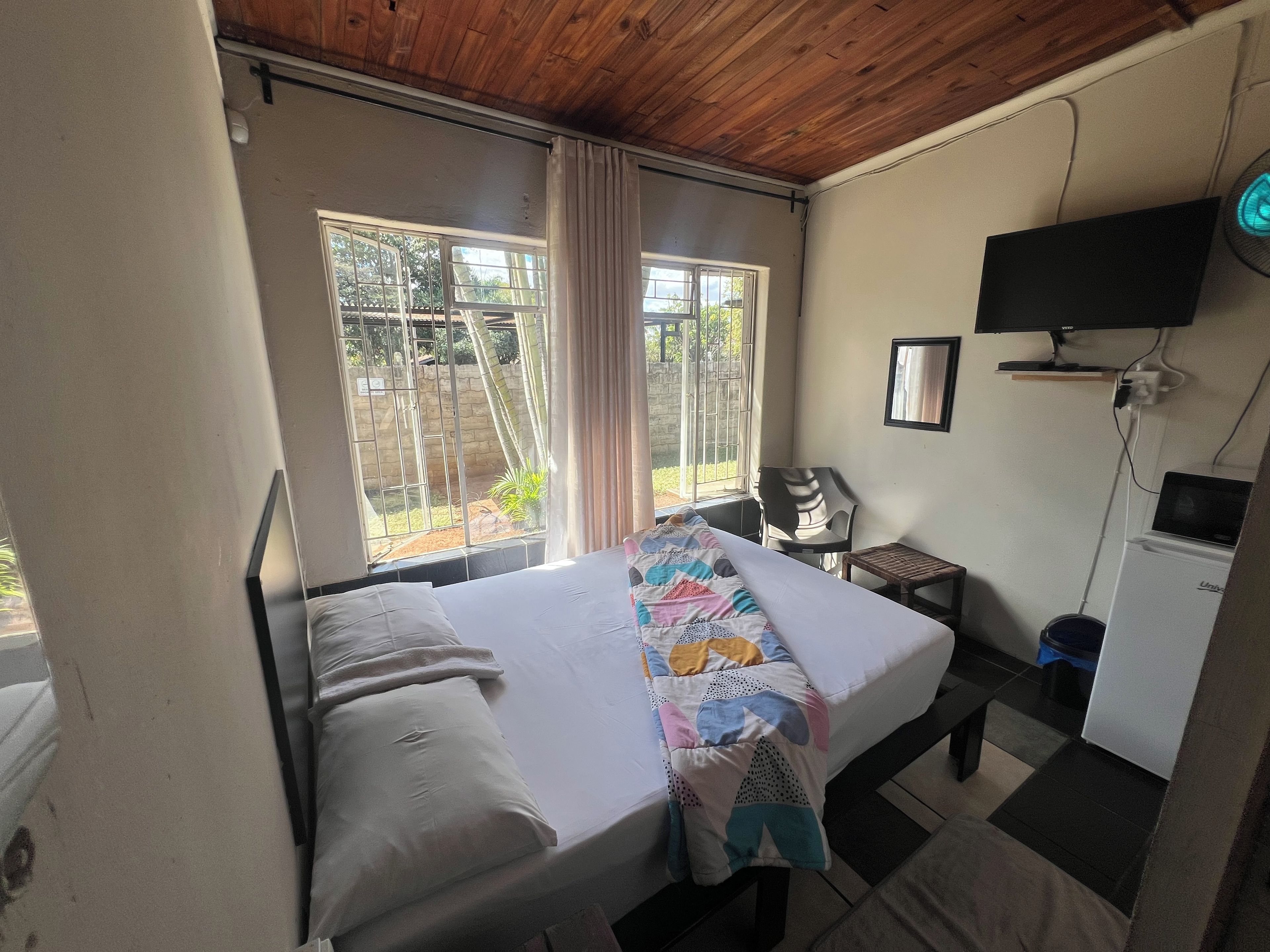 A room with a bed, a desk, a television, and a window with a view of greenery.