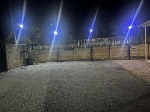 Un espacio al aire libre con suelo de grava, una valla de metal y varios postes de luz.