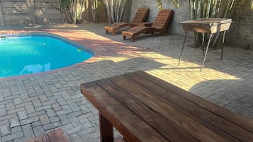 A swimming pool with lounge chairs and a barbecue grill.