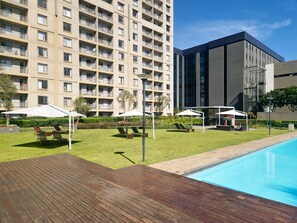 A modern hotel with a swimming pool, outdoor seating, and a well-maintained lawn. - Sandton Westpoint Luxury Apartments 158 (Sandton)
