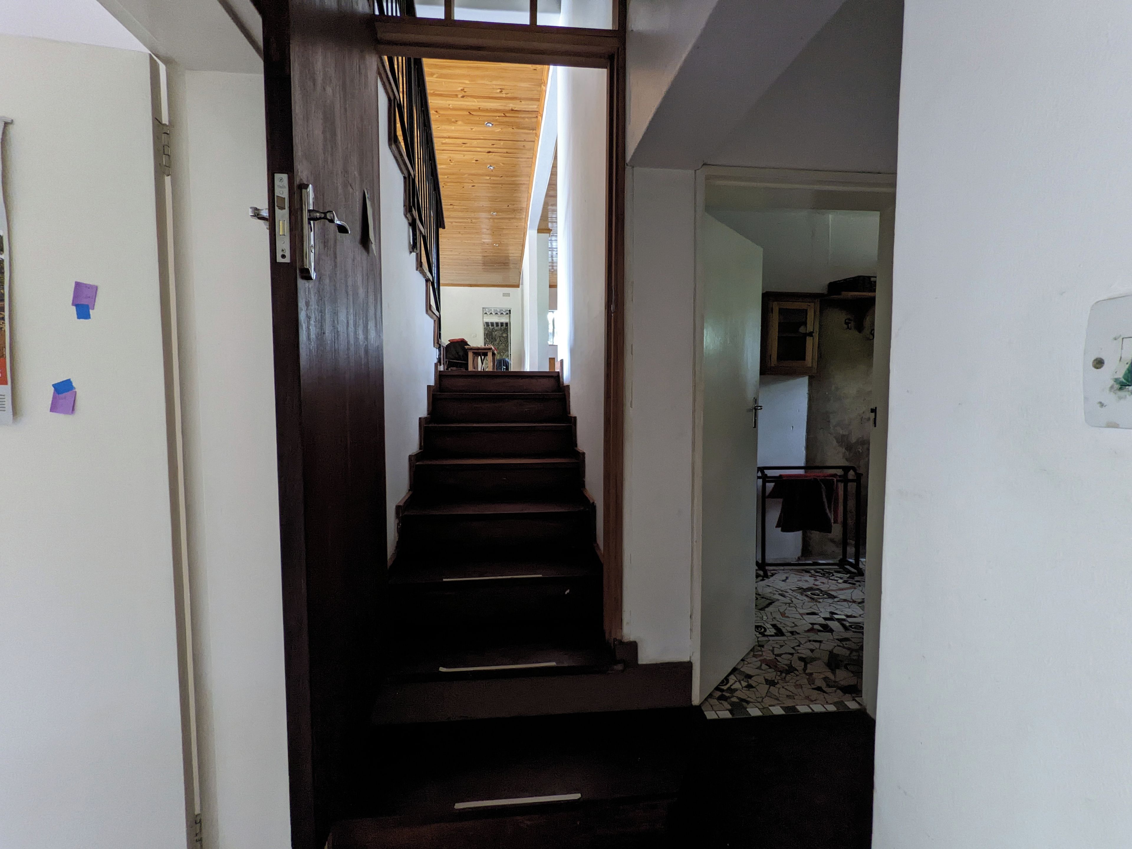 Un escalier menant à une pièce dotée d’une porte blanche, d’un plafond en bois et d’un sol carrelé.