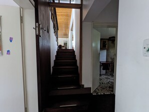 Gradi que porten a una habitació amb una porta blanca, un sostre de fusta i un paviment de rajola.
