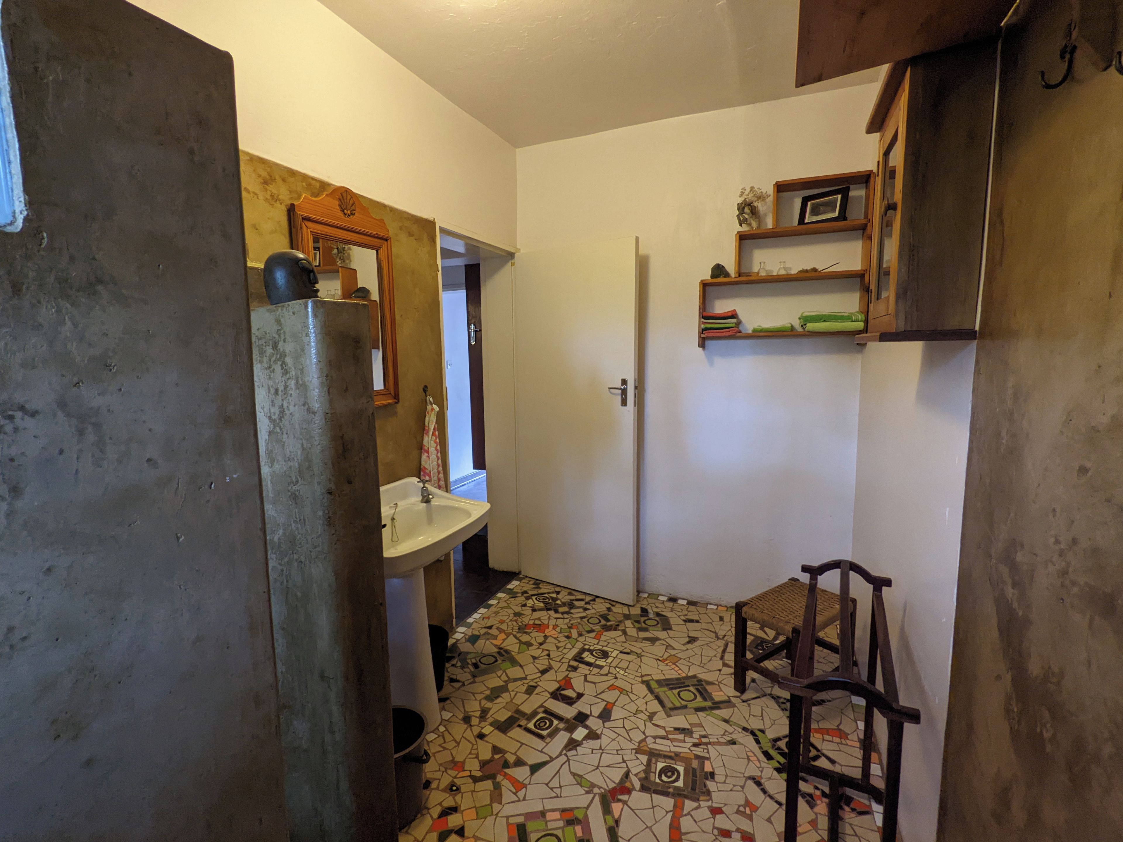 Een kleine badkamer met een wastafel, spiegel, deur en stoel.