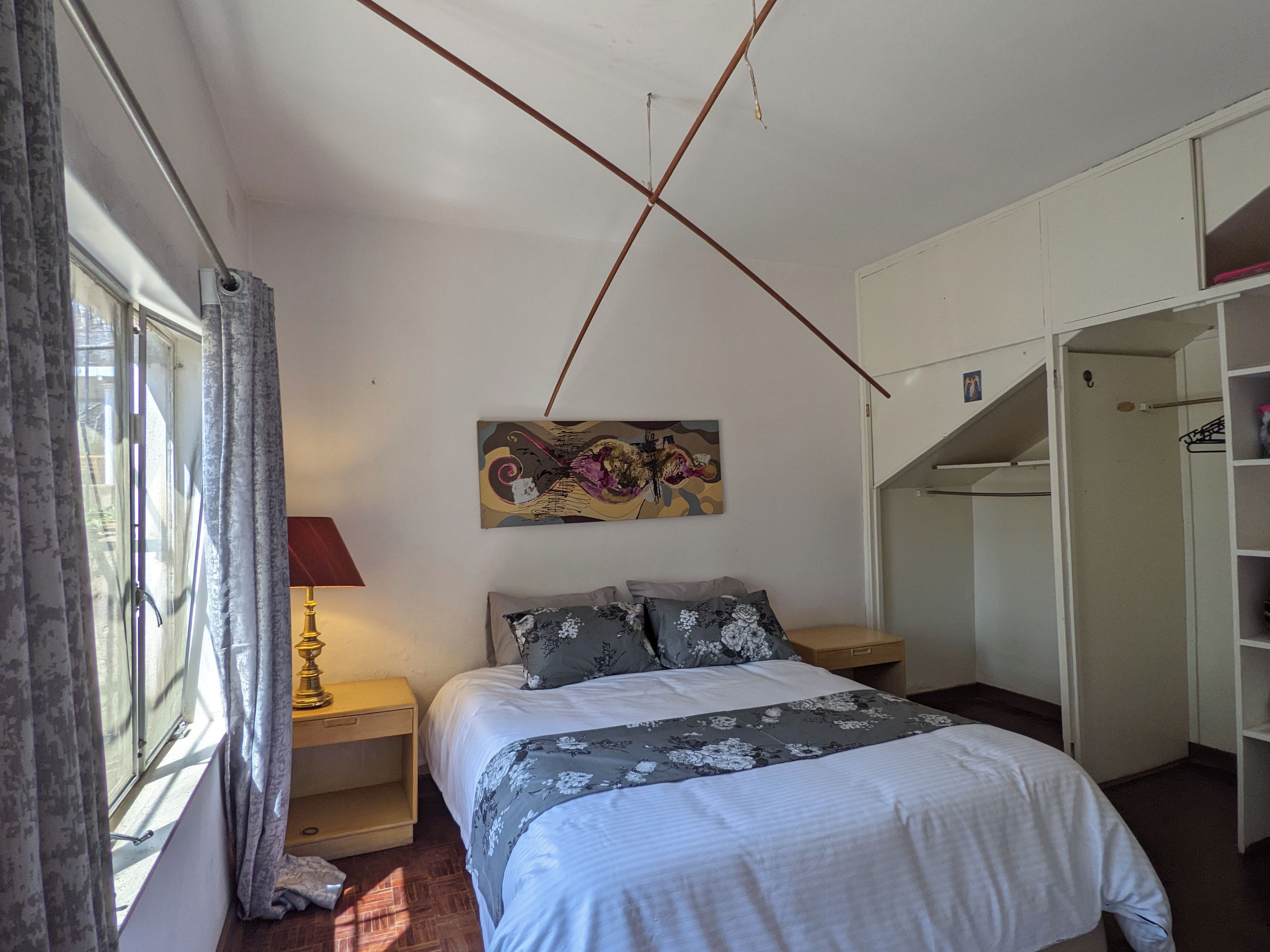 A bedroom with a bed, a nightstand, a lamp, a painting, and a wardrobe.