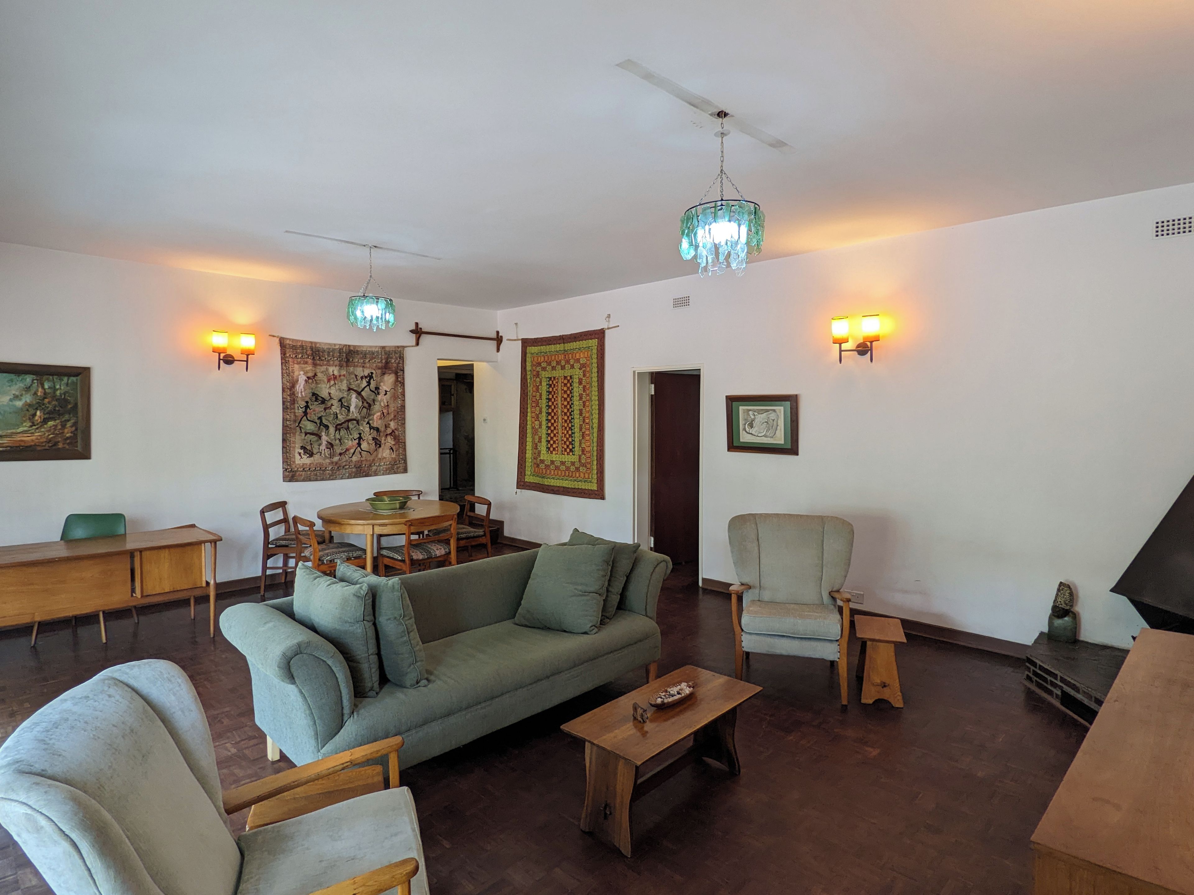 Una sala de estar con sofá, sillones, una mesa de centro, una mesa de comedor con sillas, una araña, luces de pared y obras de arte.