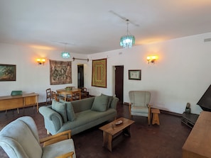 A living room with a sofa, chairs, a coffee table, a dining table with chairs, a chandelier, wall-mounted lights, and artwork.