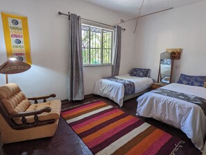 Un dormitorio con dos camas, un sofá, un felpudo a rayas, una ventana con cortinas y un espejo montado en la pared.