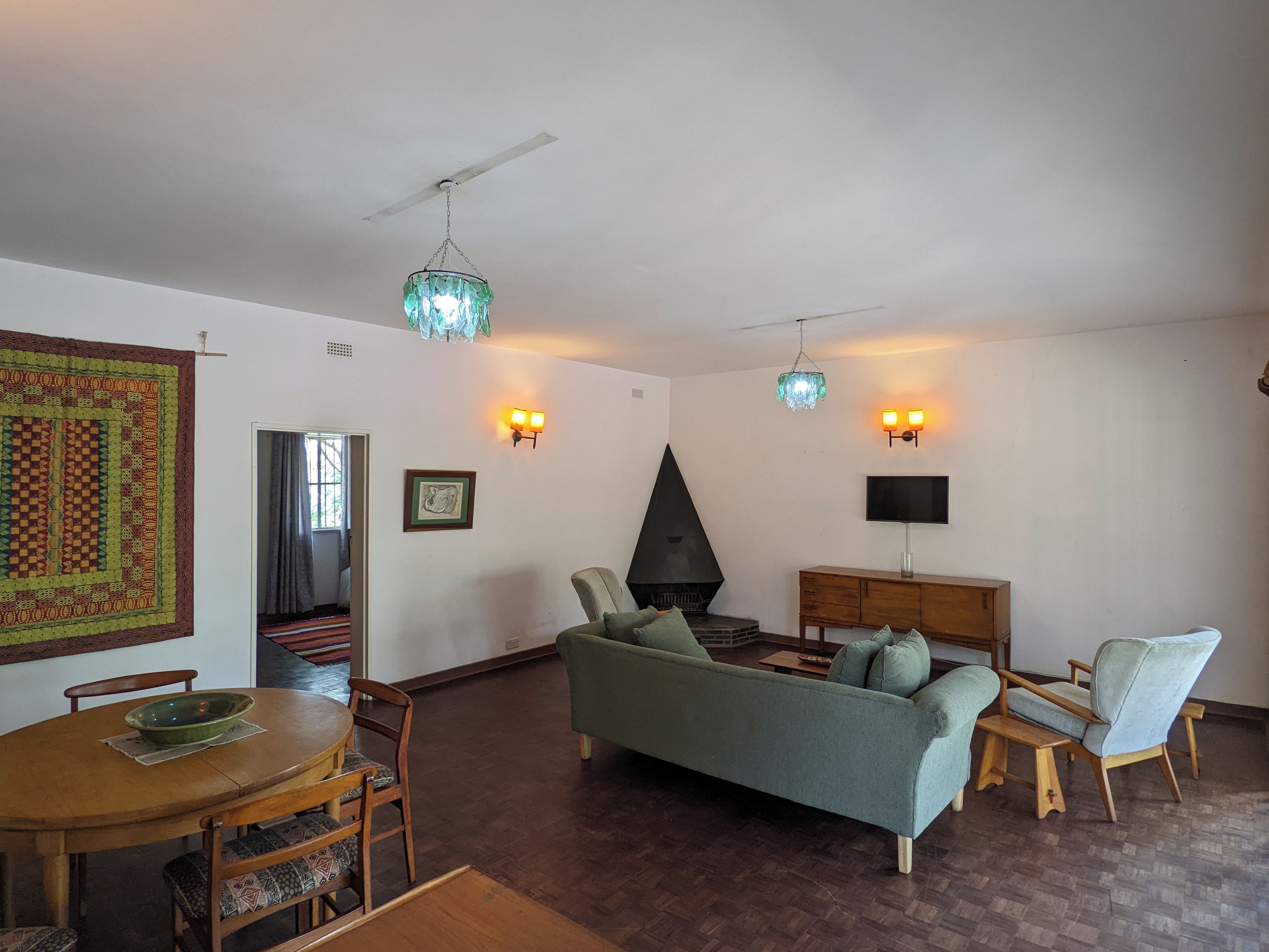A living room with a sofa, chairs, a dining table, a fireplace, and wall-mounted lights.