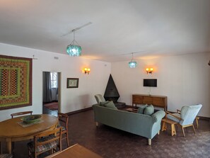 Ein Wohnzimmer mit Sofa, Sesseln, einem Esstisch, einem Kamin und Wandleuchten.