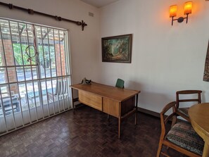 Ein Zimmer mit einem Holztisch, einem Stuhl, einem Fenster mit Metallgitter und einer Wandleuchte.