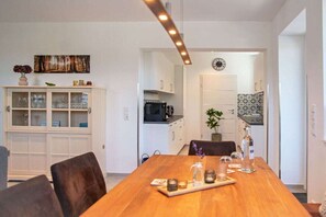 A dining area with a wooden table set for four, a cabinet with glass doors, and a kitchen visible in the background. - Black Forest jewel terrace flair (Bonndorf im Schwarzwald)