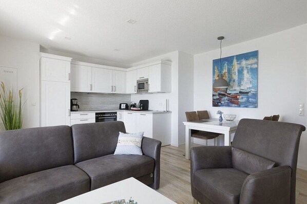 Ein moderner Wohnbereich mit einer Couch, Sesseln, einem Esstisch und einer Küche im Hintergrund.