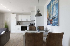 Eine moderne Küche mit weißen Schränken, ein Essbereich mit braunen Stühlen und ein Segelbootsgemälde an der Wand.