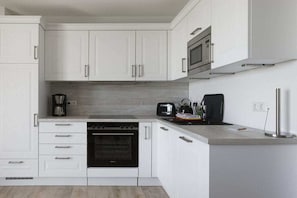 Eine moderne Küche mit weißen Schränken, einem eingebauten Backofen, einer Mikrowelle und einer Kaffeemaschine.