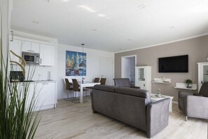 Ein modernes Wohnzimmer mit einem grauen Sofa, einem Flachbildfernseher und einem Essbereich mit einem weißen Tisch und Stühlen.