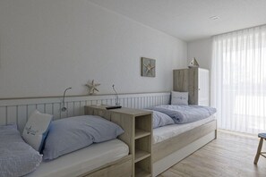 Ein Schlafzimmer mit zwei Betten, einem Holznachttisch, einer Dekoration mit Seestern und einem Fenster mit durchsichtigen Vorhängen.