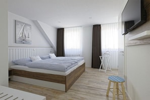 Ein modernes Schlafzimmer mit einem hölzernen Bett, einem weißen Nachttisch, einem kleinen Hocker, einem Deckenventilator und einem an der Wand befestigten Fernseher.