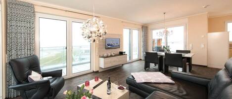A modern living room with a sofa, a coffee table with flowers, a TV, and a dining area with chairs and a table.