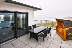 Ein Balkon mit Glastür, einem Tisch mit Stühlen und einem Rattansofa.