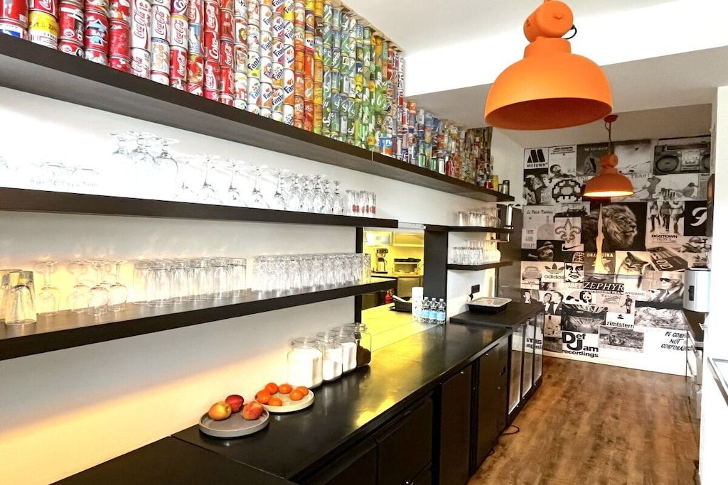 A bar area with shelves of glassware, a counter with fruits, and a wall decorated with various posters.