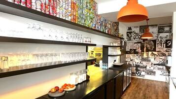 A bar area with shelves of glassware, a counter with fruits, and a wall decorated with various posters.