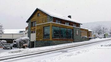 A two-story wooden house with large windows and a snow-covered roof.